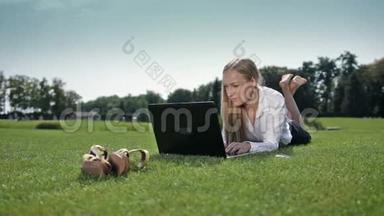 女商人拿着笔记本电脑躺在草地上